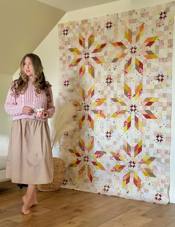 woman standing in front of a quilt top hung on a wall.